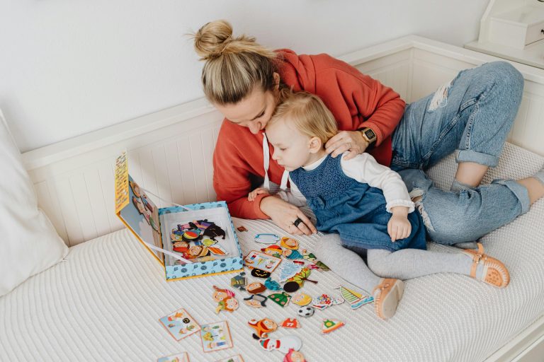 A mother and toddler playing a puzzle game on a bed.