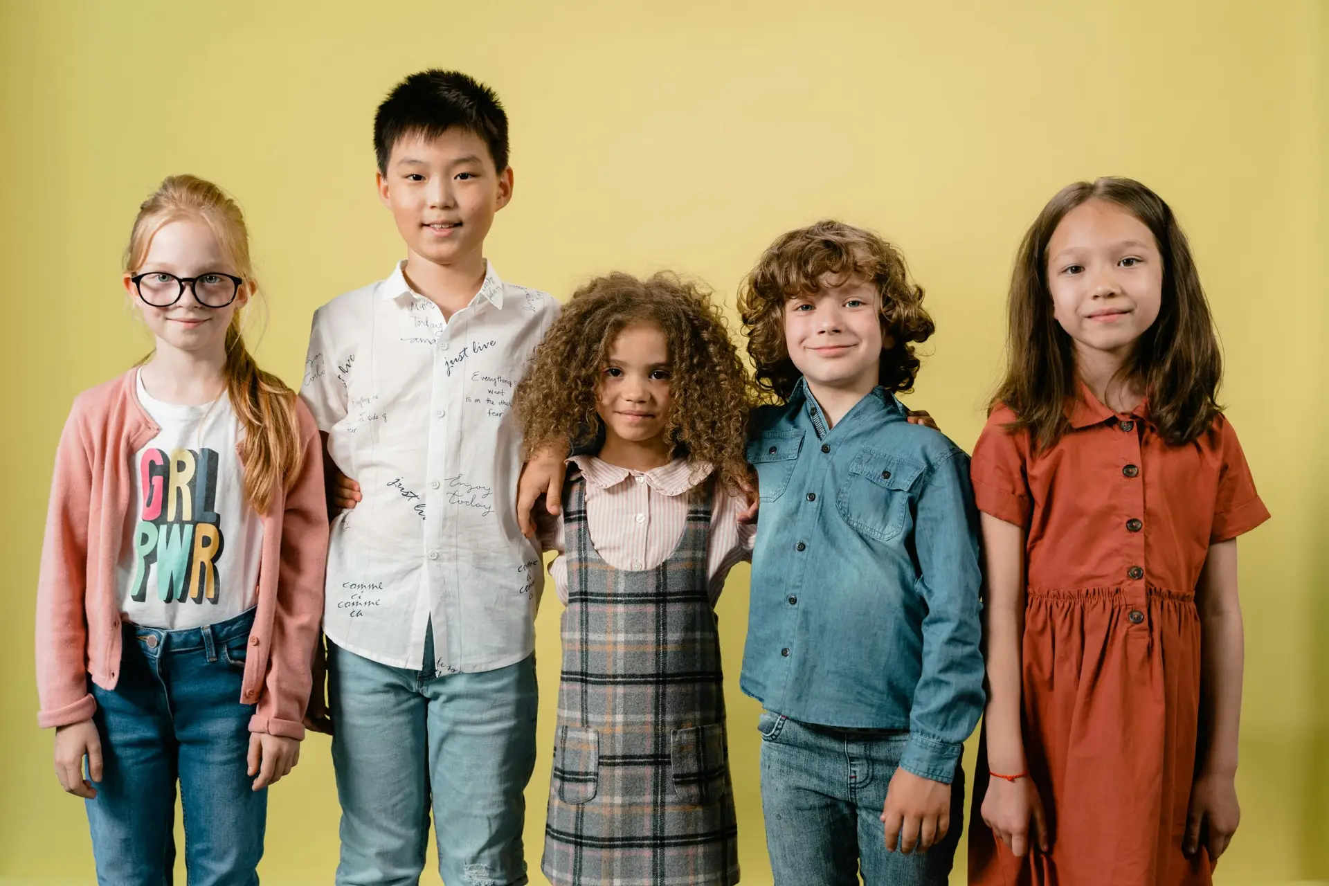 A group of diverse children stand together against a yellow backdrop