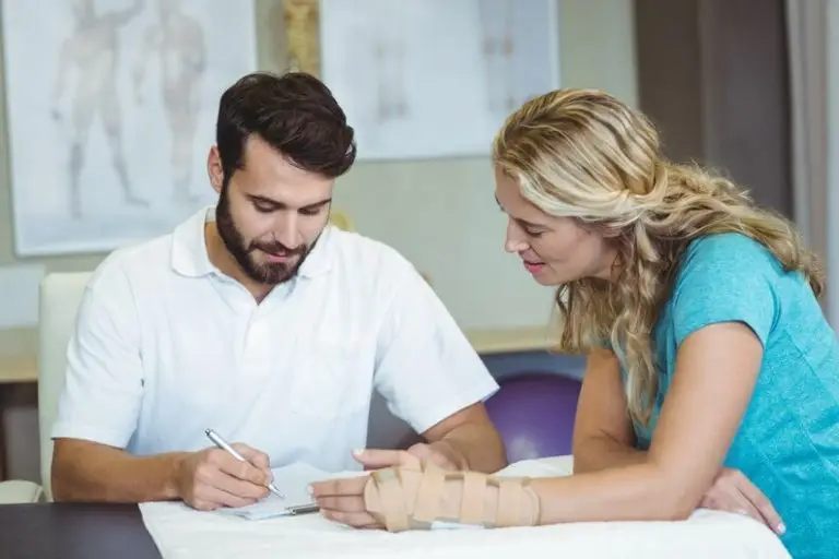 A woman with an injured write looking at some papers a man is going over with a pen.
