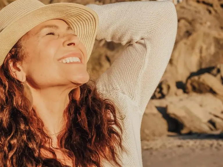 A warm image of a woman looking up to the sun and smiling. she is wearing a straw hat.
